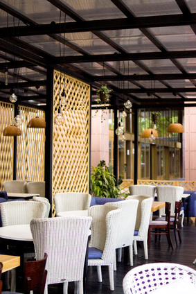 Photo d'un intérieur décoré de restaurant, sièges en osier blanc et cousins bleus, par-vue treille en bois, ampoules nues sous plafond de verre, parquet anthracite